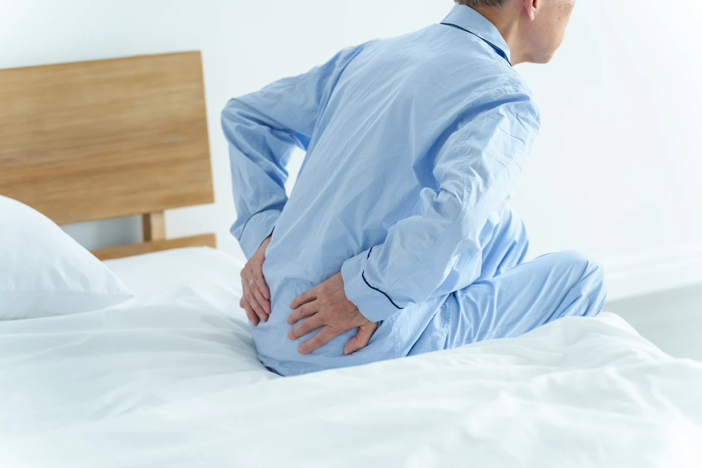 ベッドから起き上がるときに背中や腰の痛みを感じている高齢の男性（写真はイメージです）